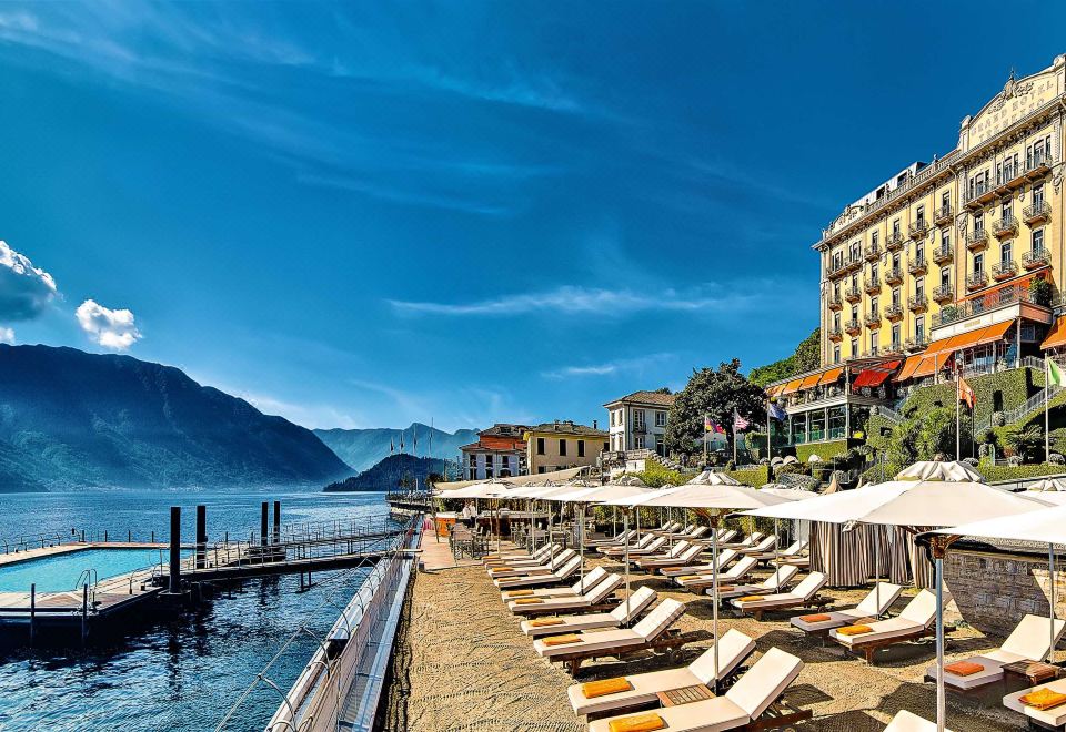 a sunny day at a beach resort with umbrellas , lounge chairs , and people enjoying the view of the water at Grand Hotel Tremezzo