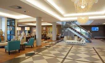 a large , well - lit hotel lobby with a checkered floor and multiple seating areas , as well as a staircase leading to the second floor at Holiday Inn Mauritius Mon Tresor