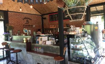 a coffee shop with a brick wall , a counter , and a bar area , where customers are enjoying their drinks and snacks at BaanSuanLeelawadee Resort Amphawa