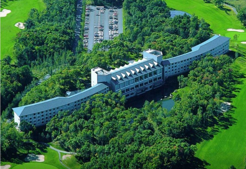 aerial view of a large hotel surrounded by green trees and grass , with cars parked in the parking lot at Hakodate-Onuma Prince Hotel