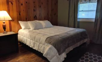 a bed with white sheets and a gray blanket is in a room with wooden walls at RiverBend Lodge
