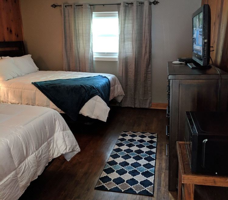 a bedroom with two beds , a tv on a stand , and a checkered rug in front of the window at RiverBend Lodge