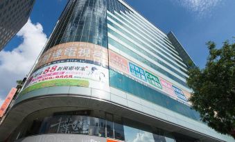 a large glass building with a curved facade and advertisements on its side , under a clear blue sky at Just Sleep Ximending