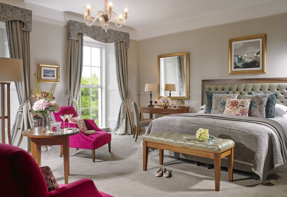 a luxurious bedroom with a large bed , pink armchairs , and a chandelier hanging from the ceiling at Actons Hotel Kinsale