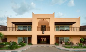 a two - story building with an arched entrance , surrounded by lush greenery and a blue sky at Jolie Ville Hotel & Spa Kings Island Luxor