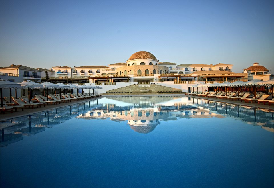 a large swimming pool is surrounded by a resort with buildings and umbrellas on the beach at Mitsis Laguna Resort & Spa