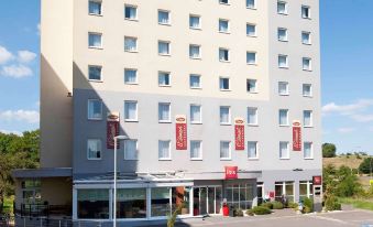 a tall hotel building with a large parking lot in front of it , surrounded by trees at Ibis Luxembourg Sud