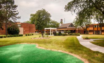 a large brick building surrounded by green grass and trees , with a green golf course in the background at Best Western Prairie Inn  Conference Center