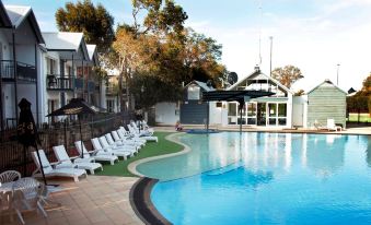 a large swimming pool with a white lounge chair and a house in the background at Mandurah Quay Resort