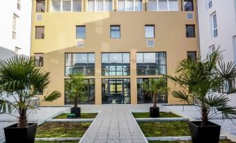 a modern building with large windows and a stone walkway leading to the entrance , surrounded by palm trees at Comfort Suites Pau Idron