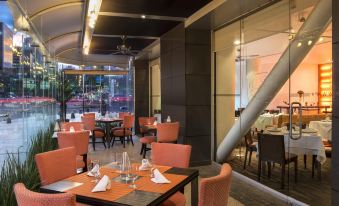 a modern restaurant with orange chairs and tables , white napkins , and a view of the city through the windows at Le Meridien Mexico City