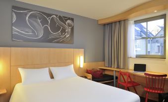 a large bed with white sheets is in a room with red chairs and a window at Ibis de Panne