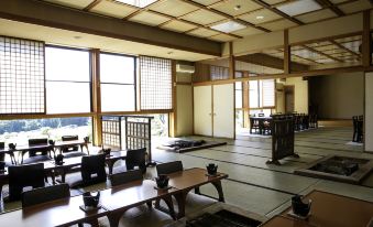 a large room with wooden tables and chairs , tatami mats on the floor , and windows that offer views of the outdoors at Ryokan Warabino