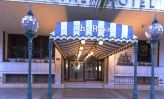 the entrance of the royal hotel with a blue and white striped awning and two lamps in front at The Royal Hotel by Coastlands Hotels & Resorts