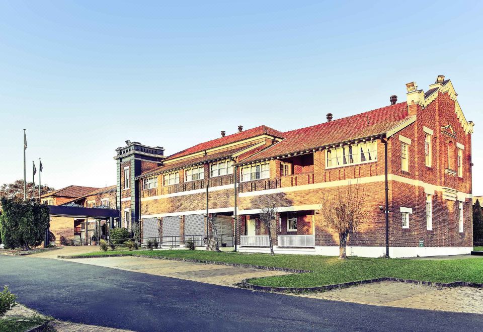 a large brick building with red roof , situated on a street corner in a city at Mercure Maitland Monte Pio