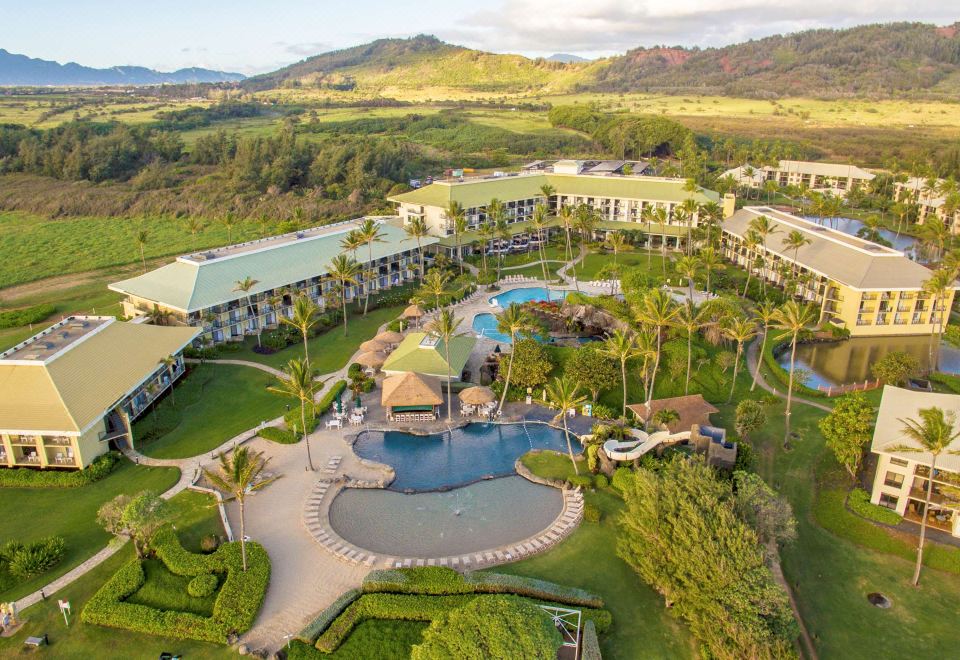 an aerial view of a resort with a large pool , surrounded by lush greenery and mountains in the background at OUTRIGGER Kaua'i Beach Resort & Spa