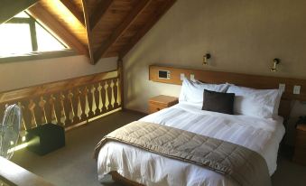 a bedroom with a large bed and a wooden headboard is shown under an angled ceiling at Alpine Lodge