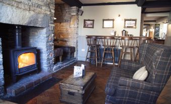 a cozy living room with a brick fireplace , a couch , and a dining table surrounded by chairs at The White Hart