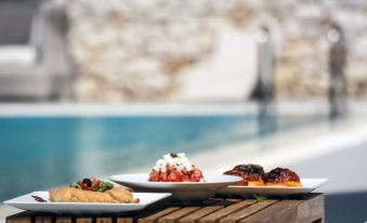 a wooden dining table with a variety of food items , including sandwiches , fruit , and a drink at Hotel Nefeli