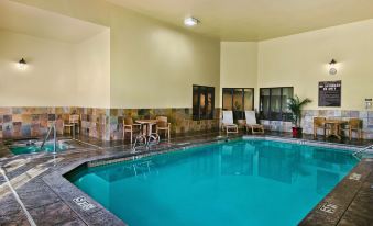 an indoor swimming pool with a clear blue water , surrounded by chairs and tables , in a well - lit room at Oxford Suites Pendleton