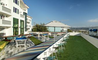 a large outdoor pool area with tables , chairs , and umbrellas is shown in front of a white building at Hotel Hermosa