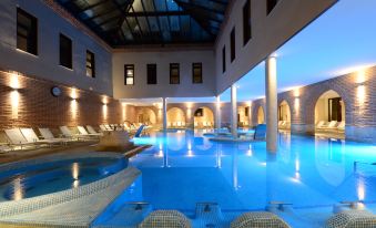 a large indoor swimming pool surrounded by lounge chairs , with several people relaxing and enjoying their time in the pool area at Castilla Termal Olmedo