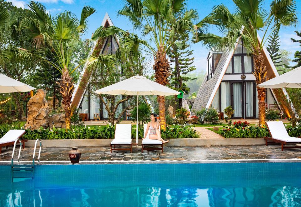 a woman is relaxing by a pool , with a lounge chair and an umbrella nearby at Bai Dinh Garden Resort & Spa