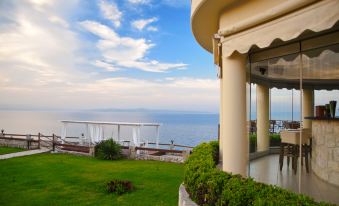 a large white house overlooking the ocean , with a view of the water in the background at Blue Bay Halkidiki