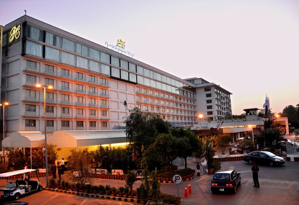 a large hotel building with many windows , surrounded by a parking lot and trees , during sunset at Pearl Continental Hotel, Lahore