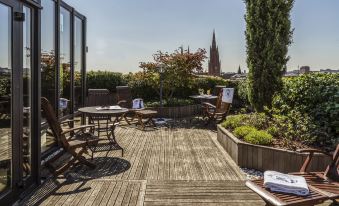 a rooftop patio with wooden decking , surrounded by greenery , and offering a view of a cathedral in the distance at Hotel Nassauer Hof