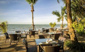 an outdoor dining area overlooking the ocean , with tables and chairs arranged for guests to enjoy their meal at Robinson Khao Lak