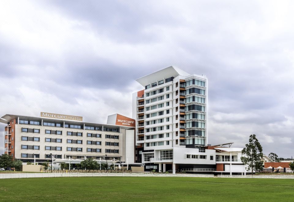 a large white building with many windows is surrounded by a grassy field and trees at Mercure Sydney Liverpool