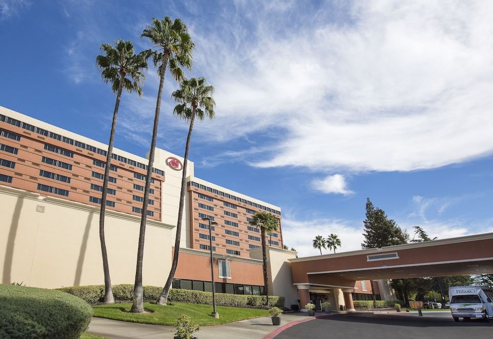 a large hotel with palm trees and a blue sky , surrounded by buildings and trees at Hilton Concord