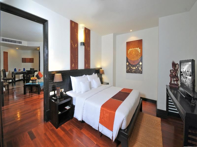 a large bed with white linens and an orange throw blanket is in a room with wooden floors at Tara Angkor Hotel