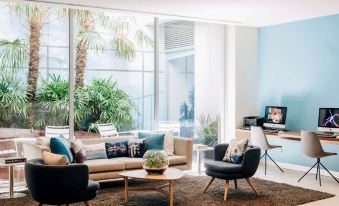 a modern living room with a large window , couches , and chairs arranged around a coffee table at Saint Kilda Beach Hotel, an EVT hotel - Formerly Rydges St Kilda