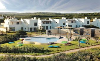 a large white house surrounded by grass and trees , with a swimming pool in the background at Martinhal Sagres Beach Family Resort Hotel