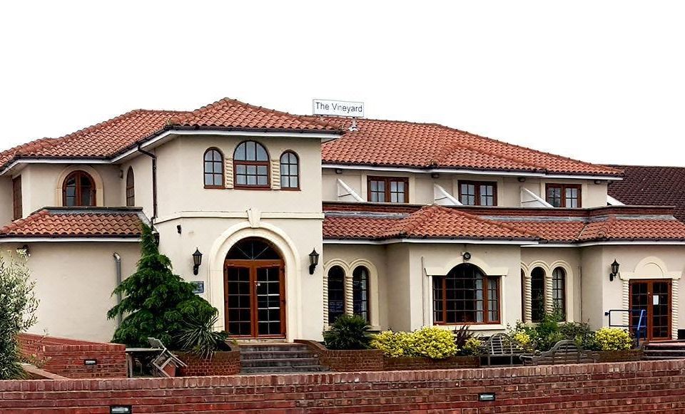 a large , white house with a red tile roof and arched windows is shown in front of a brick wall at Skylark Hotel