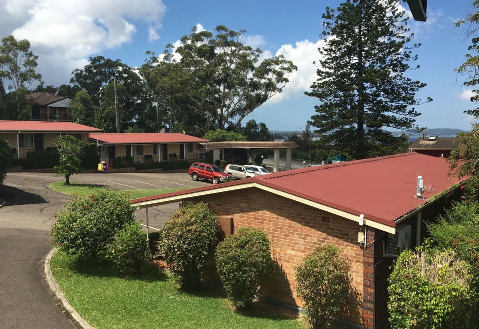 a motel with a red roof and cars parked in front , surrounded by trees and grass at Waterview Gosford Motor Inn