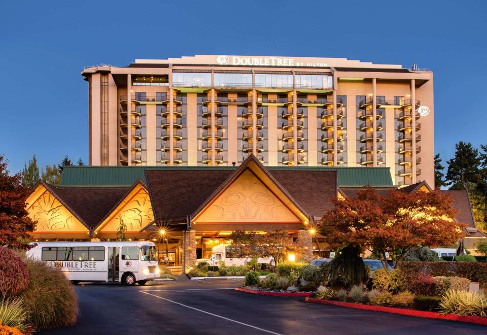 a large hotel building with a parking lot in front of it , surrounded by trees at DoubleTree by Hilton Seattle Airport