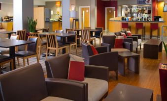 a modern lounge area with brown leather chairs and wooden tables , creating a comfortable seating arrangement at Holiday Inn Express Droitwich Spa