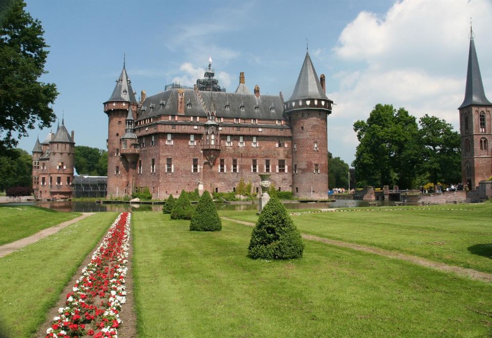 a large red brick castle surrounded by a lush green lawn , with trees and bushes in the background at Fletcher Hotel Restaurant Loosdrecht-Amsterdam