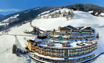 an aerial view of a snow - covered ski resort with multiple buildings , including a hotel , surrounded by trees and mountains at Alpin Panorama Hotel Hubertus