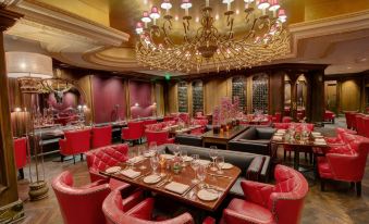a large , well - lit dining room with multiple tables and chairs , red leather couches , and a chandelier at Garden City Hotel