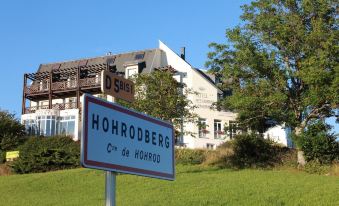 "a sign for "" hohoberg "" and a building in the background , with trees and a clear sky visible" at Hôtel Panorama