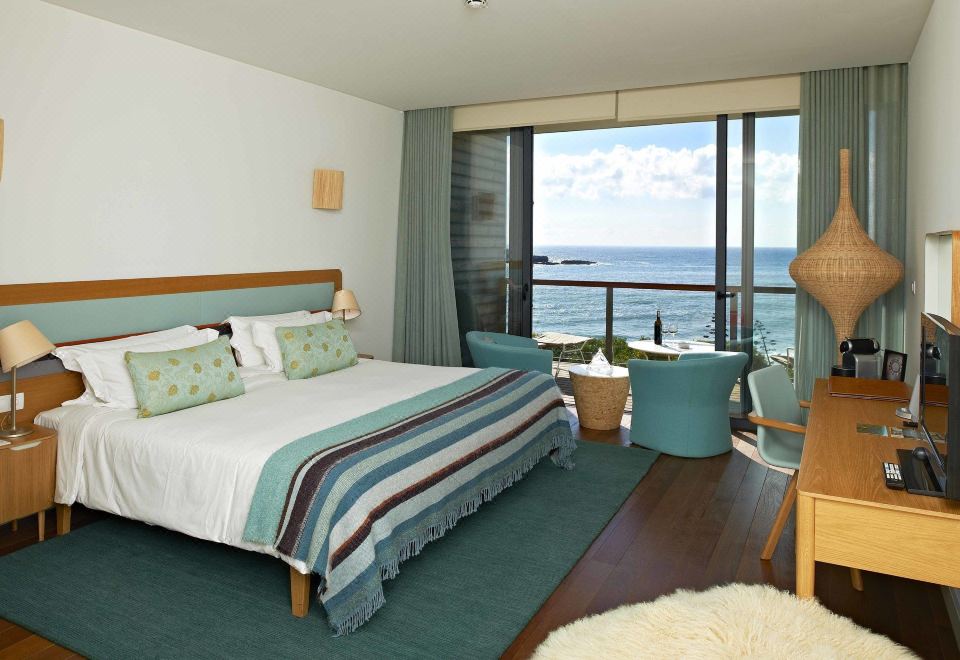 a hotel room with a large bed , a chair , and a window overlooking the ocean at Martinhal Sagres Beach Family Resort Hotel