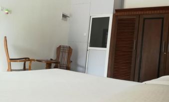 a bed with a white sheet and two chairs in front of it , next to a wooden door at Sea Breeze