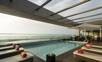 a large swimming pool with a wooden deck and lounge chairs is surrounded by a glass roof at Hotel Baia