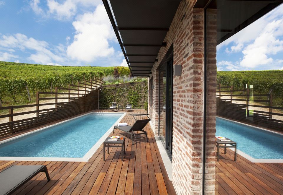 a brick house with a wooden deck surrounding it , where two people are relaxing by the pool at Arborina Relais