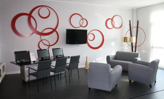 a modern living room with a red circle design on the wall , a gray couch , and multiple computer monitors at Idea Hotel Milano Malpensa Airport