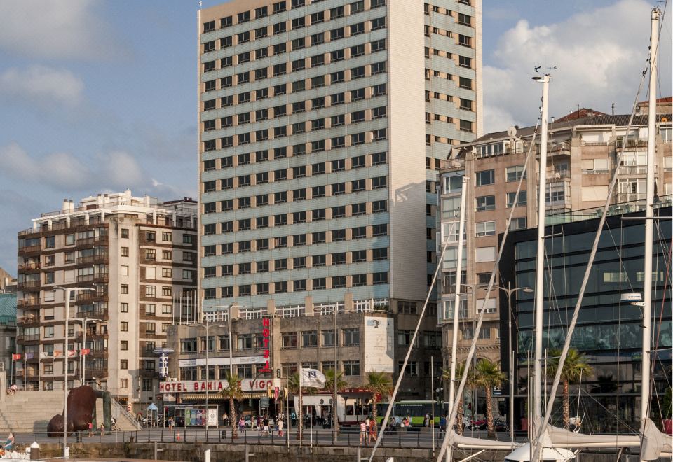a large building with many windows is surrounded by tall buildings and sailboats in the water at Sercotel Hotel Bahia de Vigo
